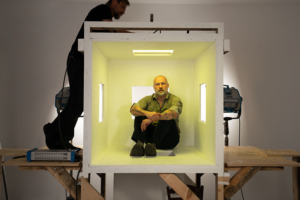 Zdjęcie przedstawia mężczyznę siedzącego w sześcianie - planowanej instalacji. 